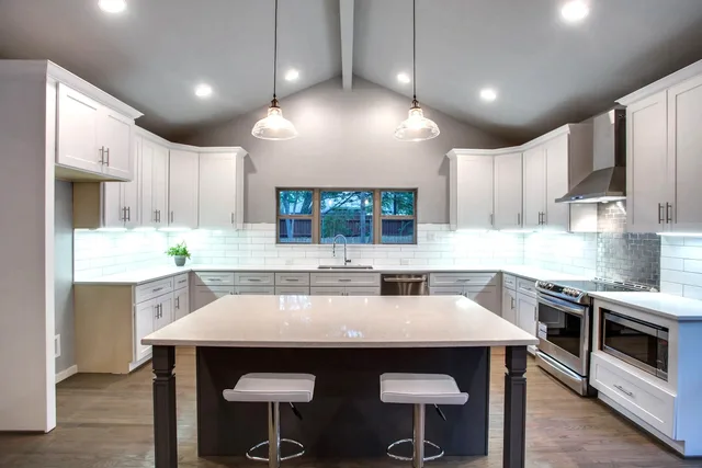 White kitchen with a large island, two stools, pendant lights and a vaulted ceiling.